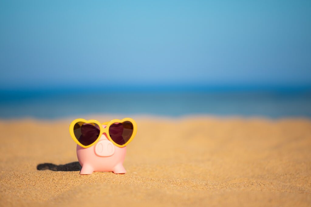 Piggybank on the beach against sea and sky background. Savings for summer travel and vacation concept